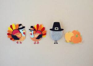 Four various Thanksgiving crafts for kids including; two multicolored turkeys, one gray egg with a black top hat, and a combination of three pumpkins, two orange, one yellow.