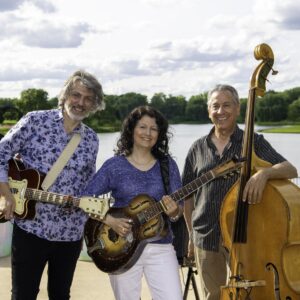 Donna Herula Trio carrying their instruments, in front of a lake. 