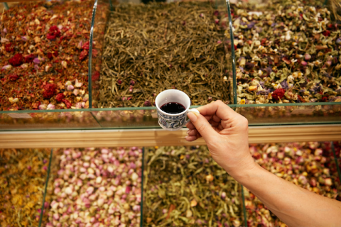 a hand holding a cup of coffee over a table of herbs