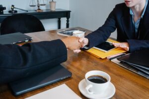two people in suits shaking hands across a table.